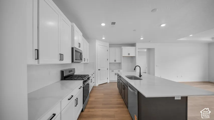 Modern kitchen featuring white shaker-style cabinetry, a contrasting dark island, stainless steel appliances, and wood-finish flooring