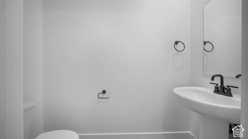 Pedestal sink with a matte black faucet, coordinating towel rings, and a wall-mounted mirror