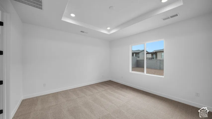Bright room featuring a tray ceiling with recessed lighting, neutral carpeting, white baseboards, and a dual-pane window