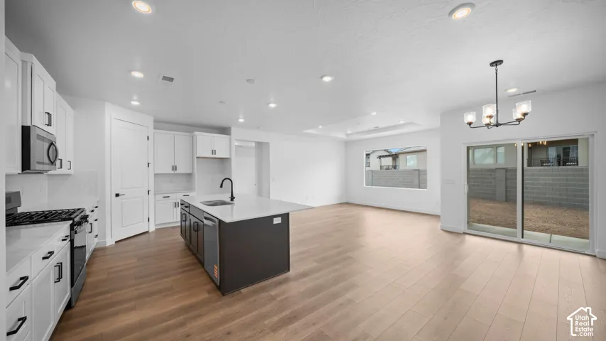 Open-concept living space featuring wood-finish flooring, a contemporary kitchen island with a white countertop and dark cabinetry, white shaker-style kitchen cabinets, stainless steel appliances, and a sliding glass door providing outdoor access