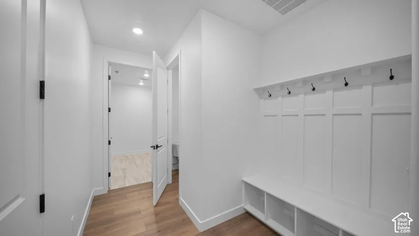 White mudroom featuring built-in bench seating with storage cubbies, integrated paneling with coat hooks, wood-finish flooring, and recessed lighting