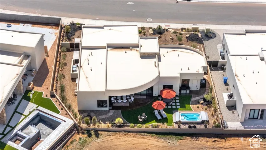 Curved modern architecture with a flat roofline, artificial turf lawn, built-in spa, expansive patio, and integrated landscaping