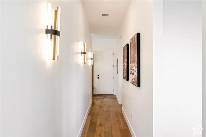 Hardwood flooring, white painted walls, white door with black hardware, recessed lighting, and modern sconce lighting