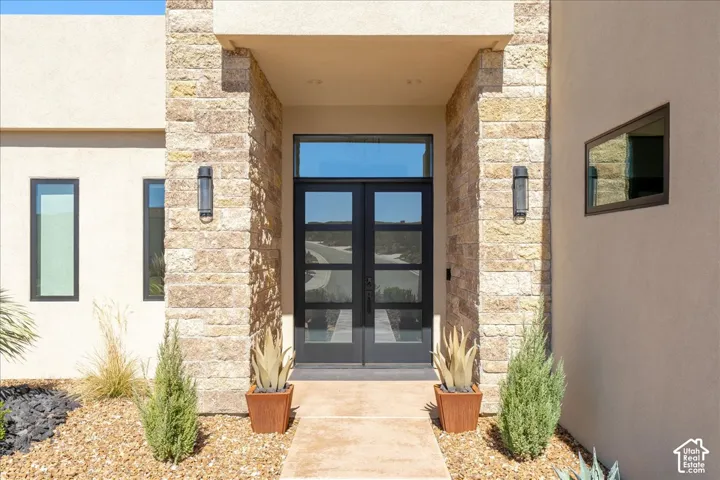 Modern entry featuring a double glass-panel door, transom window, and stone column accents