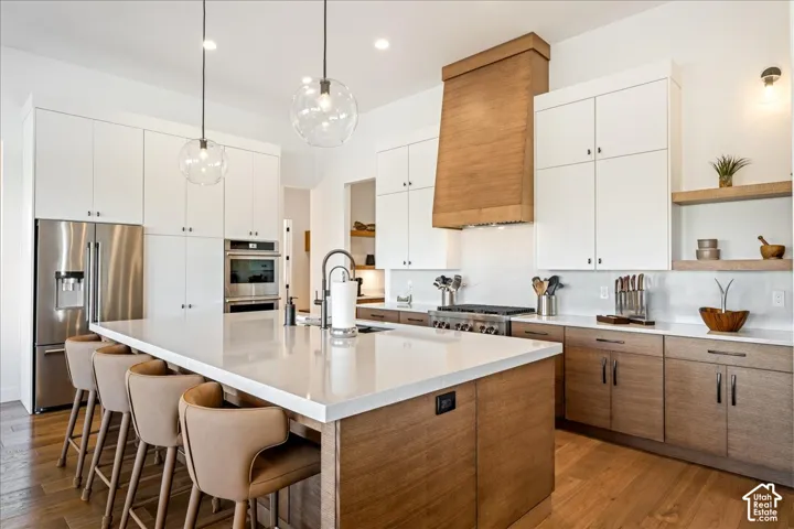Expansive kitchen island with a light-toned countertop, stainless steel appliances, wood-finish flooring, and two-tone cabinetry with open shelving