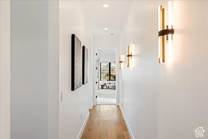 Hardwood flooring, recessed lighting, and modern wall sconces illuminate this hallway