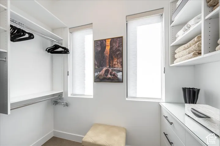 Built-in shelving, hanging rods, two windows with roller shades, and a glossy white vanity with dark drawer pulls