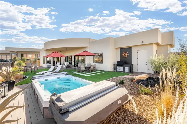 Spacious patio featuring a built-in spa, wood-finish decking, and an outdoor kitchen area with a grill