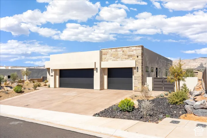 Contemporary exterior with stacked stone accents, two-car garage with dark paneled doors, stucco finish, and a paved driveway