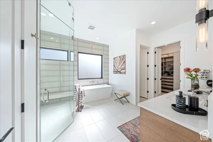 Freestanding soaking tub, glass-enclosed shower, dual vanity with wood-finish cabinetry, and recessed lighting