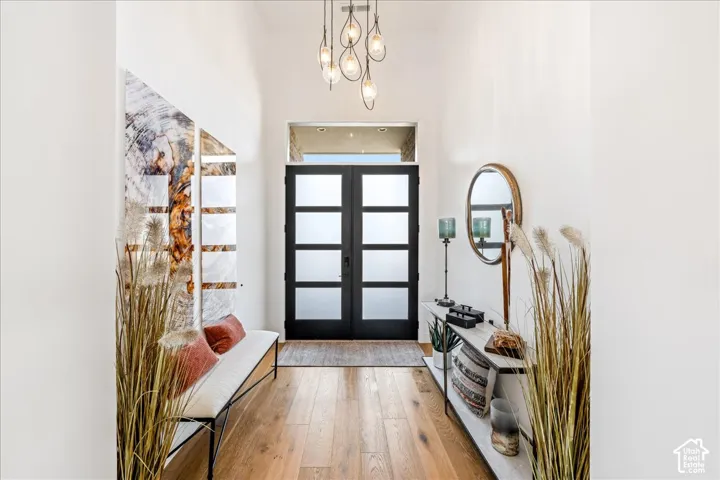 Entryway featuring wood-finish flooring, a contemporary chandelier, and a black double-door entry with frosted glass panels