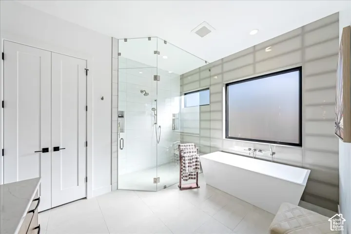 Spacious bath featuring a freestanding soaking tub, expansive window, and frameless glass shower enclosure