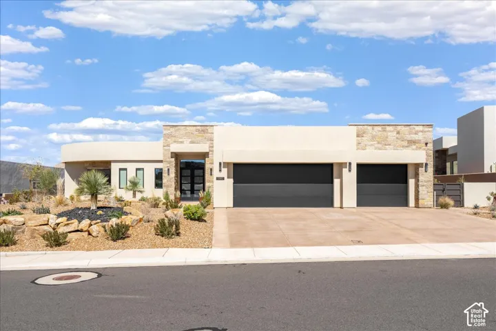 Modern desert-style architecture with a stone-clad entry, an expansive two-car garage, and stucco exterior