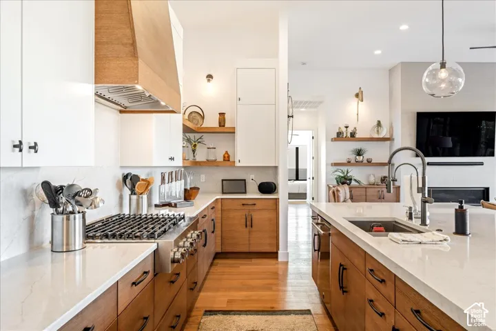 Contemporary kitchen featuring wood-finish flooring, white countertops, wood-finish lower cabinetry, white upper cabinetry, and a stainless steel gas range with a wood-finish hood