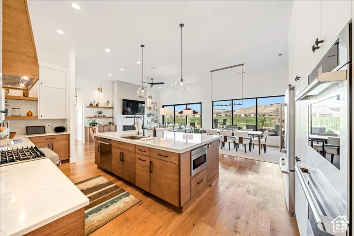 Spacious kitchen featuring a large central island with sink, wood-finish flooring, built-in stainless steel appliances, and a gas cooktop