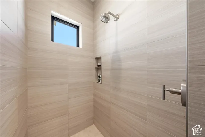Shower with light-toned rectangular wall tiles, built-in recessed shelf, fixed window, and brushed metal showerhead