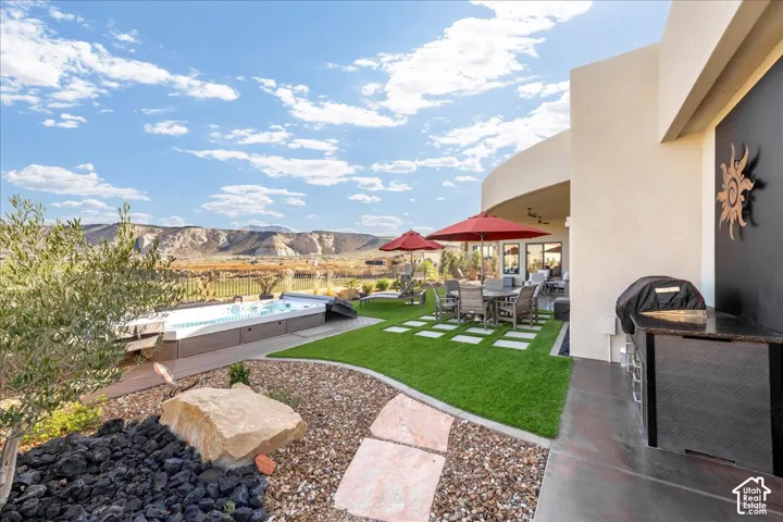 Expansive backyard featuring a built-in swim spa, artificial turf, flagstone-style patio pavers, a built-in outdoor kitchen with granite-style countertop, and a stucco exterior
