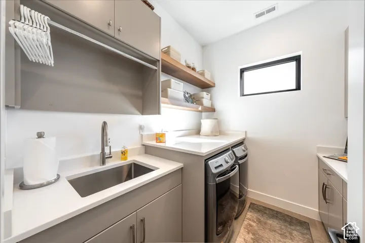 Integrated laundry appliances, stainless steel sink with a high-arc faucet, light-colored countertops, wood-finish open shelving, and upper cabinetry