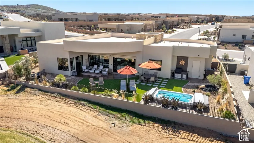 Stucco exterior with a flat roofline, featuring large glass doors, a manicured lawn, and a built-in outdoor swim spa