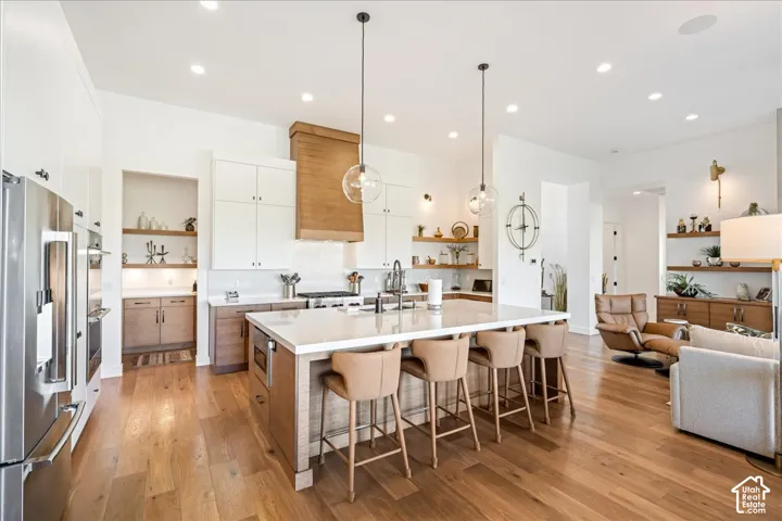 Gourmet kitchen with stainless steel appliances, a large central island with seating, wood-finish flooring, and recessed lighting