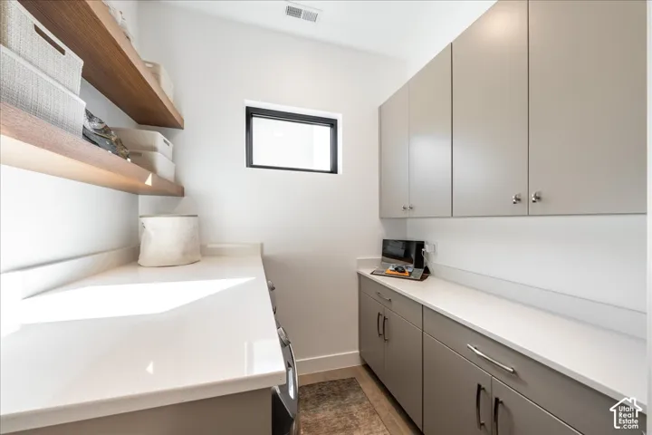 White countertops, wood-finish open shelving, gray cabinetry, and a black-framed window