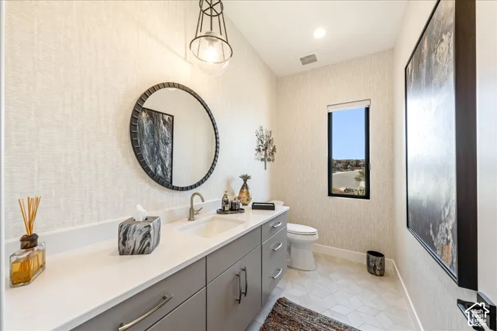 Neutral textured wallpaper, contemporary vanity with white countertop, integrated rectangular sink, round framed mirror, and geometric floor tiling