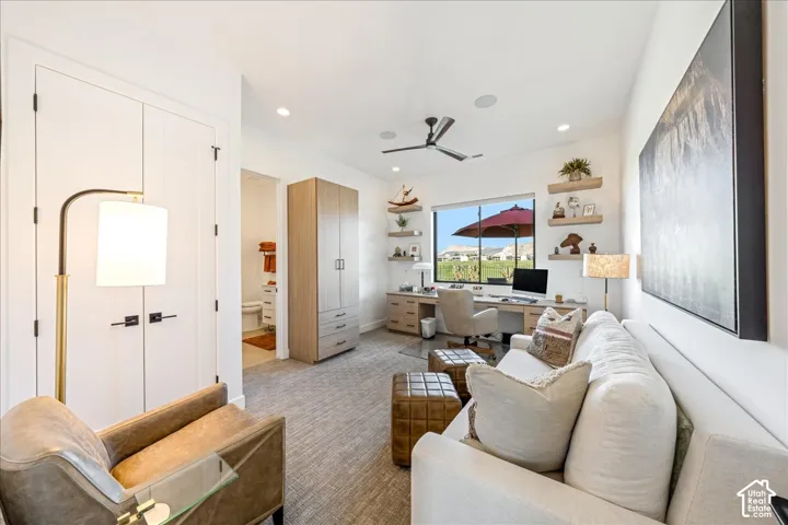 Recessed lighting illuminates the room, featuring a built-in desk, floating shelves, and a ceiling fan