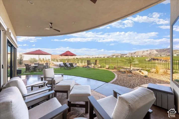 Curved patio featuring recessed lighting, a ceiling fan, sliding glass doors, a manicured lawn, and expansive desert and mountain scenery