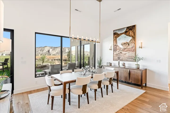 Dining space with wood-finish flooring, high ceilings, large black-framed windows, and a long linear chandelier