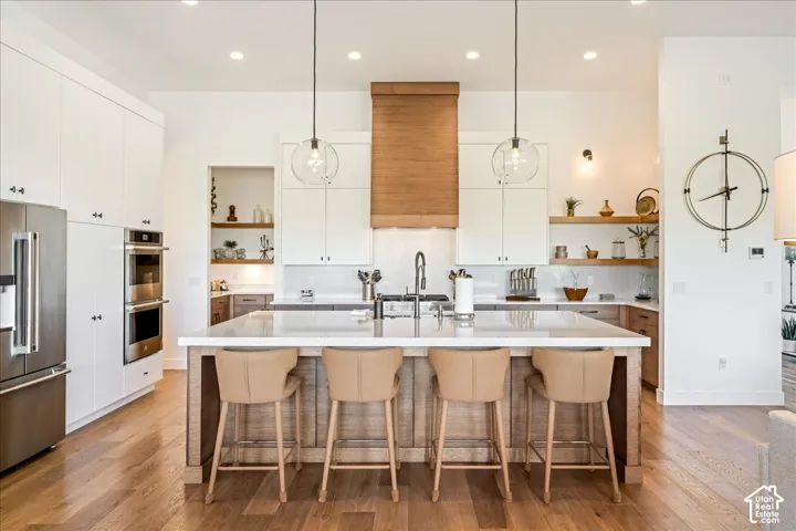 Gourmet kitchen featuring a large central island, stainless steel double ovens, a built-in refrigerator, wood-finish flooring, and a decorative range hood