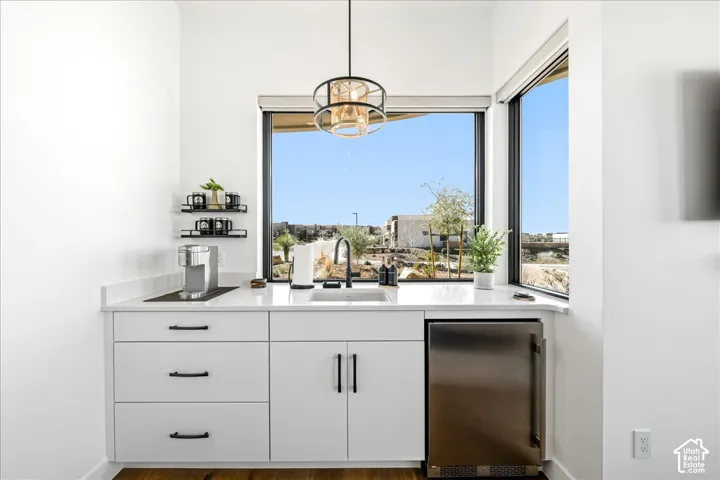 Built-in beverage refrigerator, white cabinetry with dark pulls, under-mount sink with a matte black faucet, and a contemporary pendant light fixture