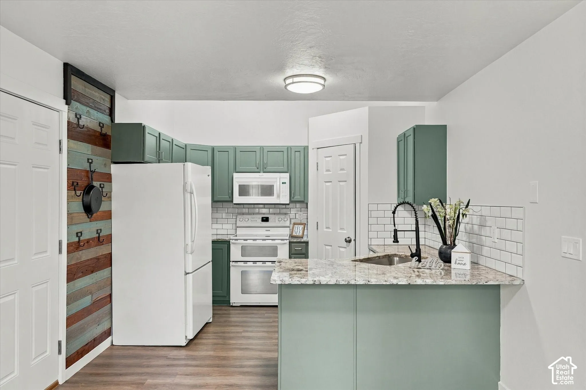 Kitchen featuring wood-finish flooring, white appliances, subway tile backsplash, and green cabinetry