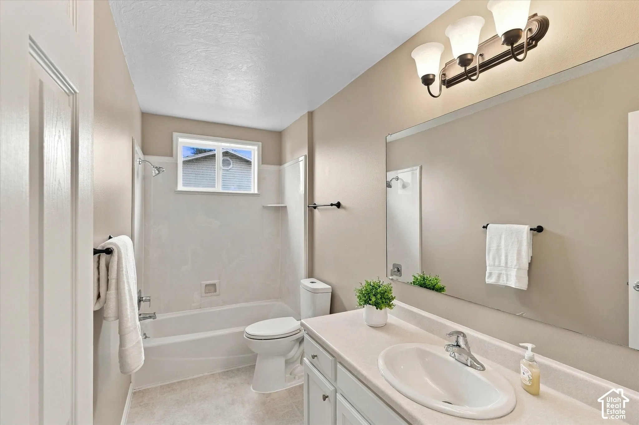 Bathroom featuring a single vanity, large wall mirror, built-in tub with shower, and an overhead lighting fixture
