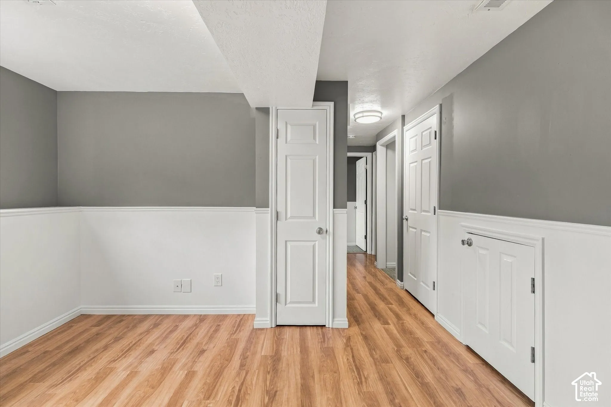 Wood-finish flooring, white wainscoting, neutral gray walls, white panel doors, and recessed ceiling lighting