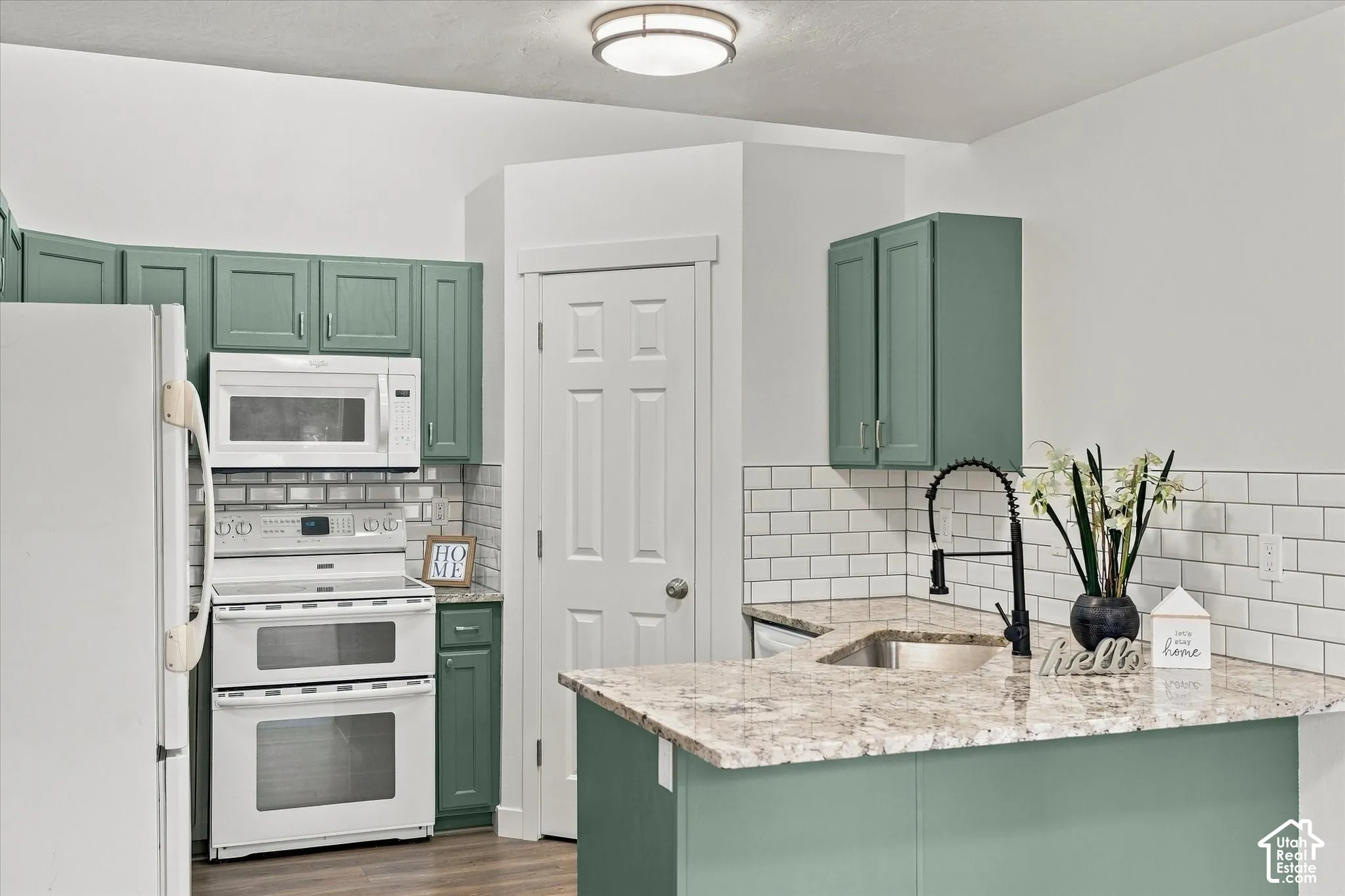 Kitchen featuring sage green cabinetry, white subway tile backsplash, light-colored stone-finish countertops, and a black gooseneck faucet