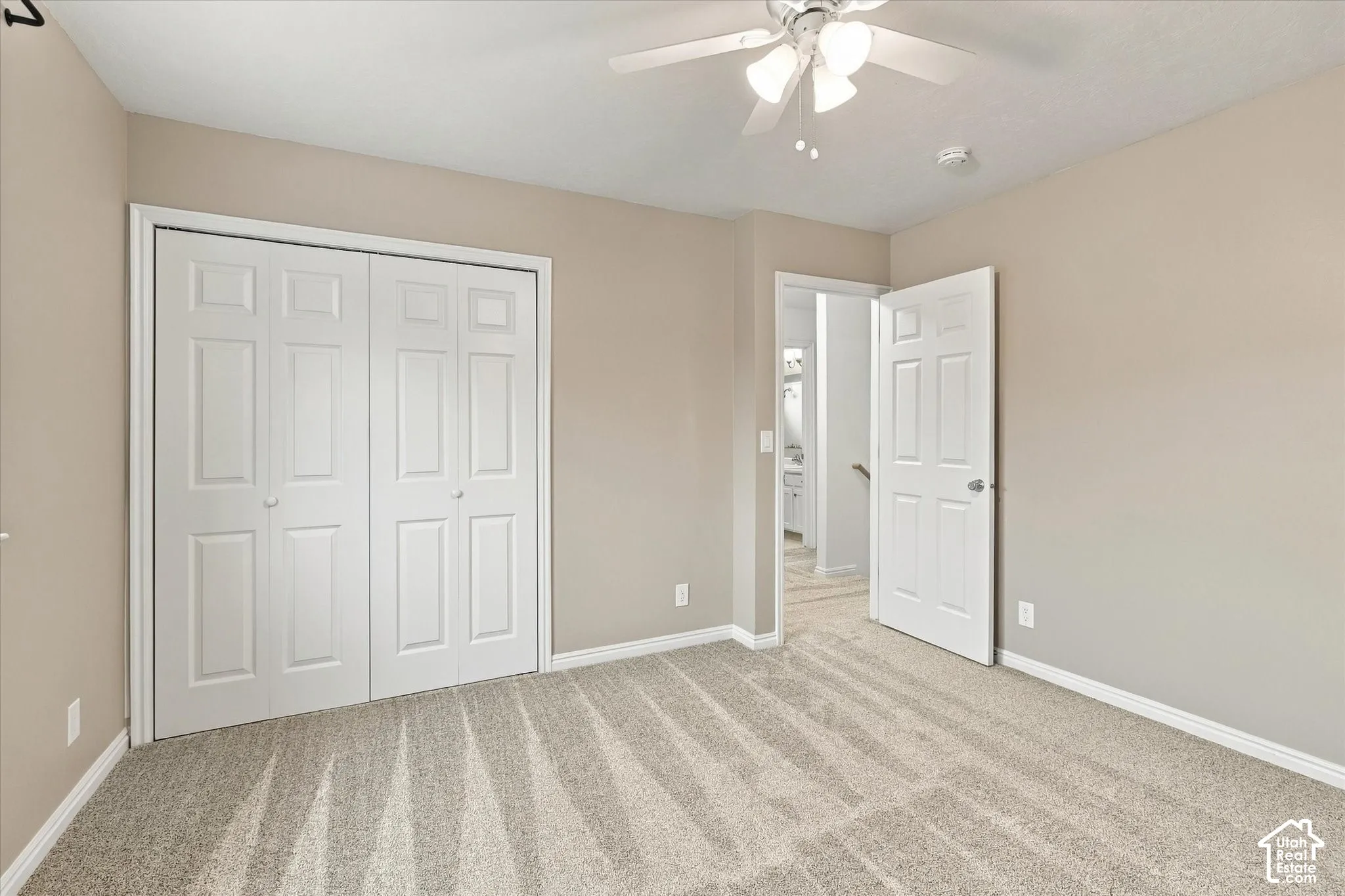 Neutral-toned walls, plush carpeting, white bi-fold closet doors, and a ceiling fan with integrated lighting