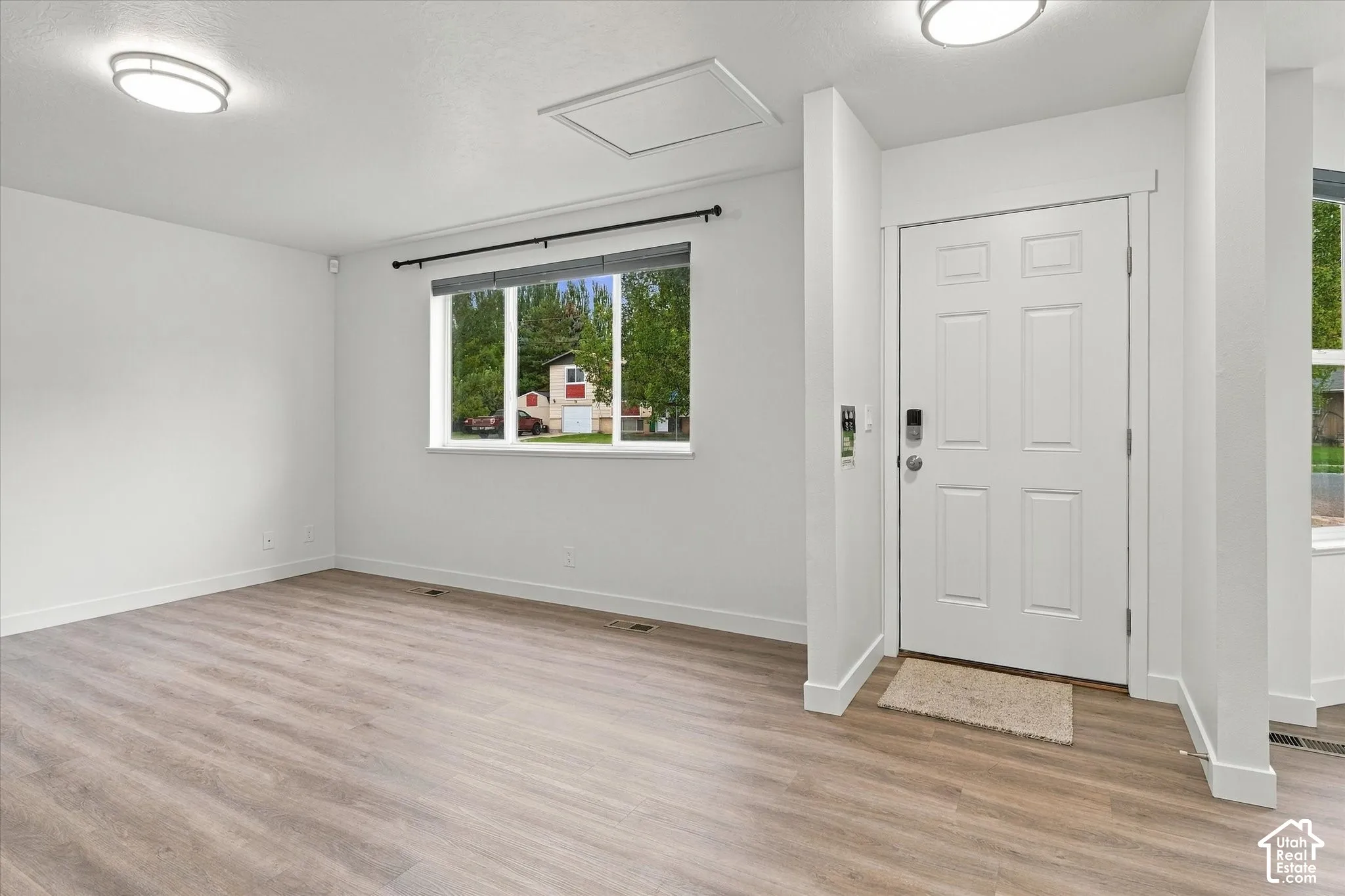 Spacious room with wood-finish flooring, recessed lighting, a multi-pane window, and a panel door with smart lock hardware