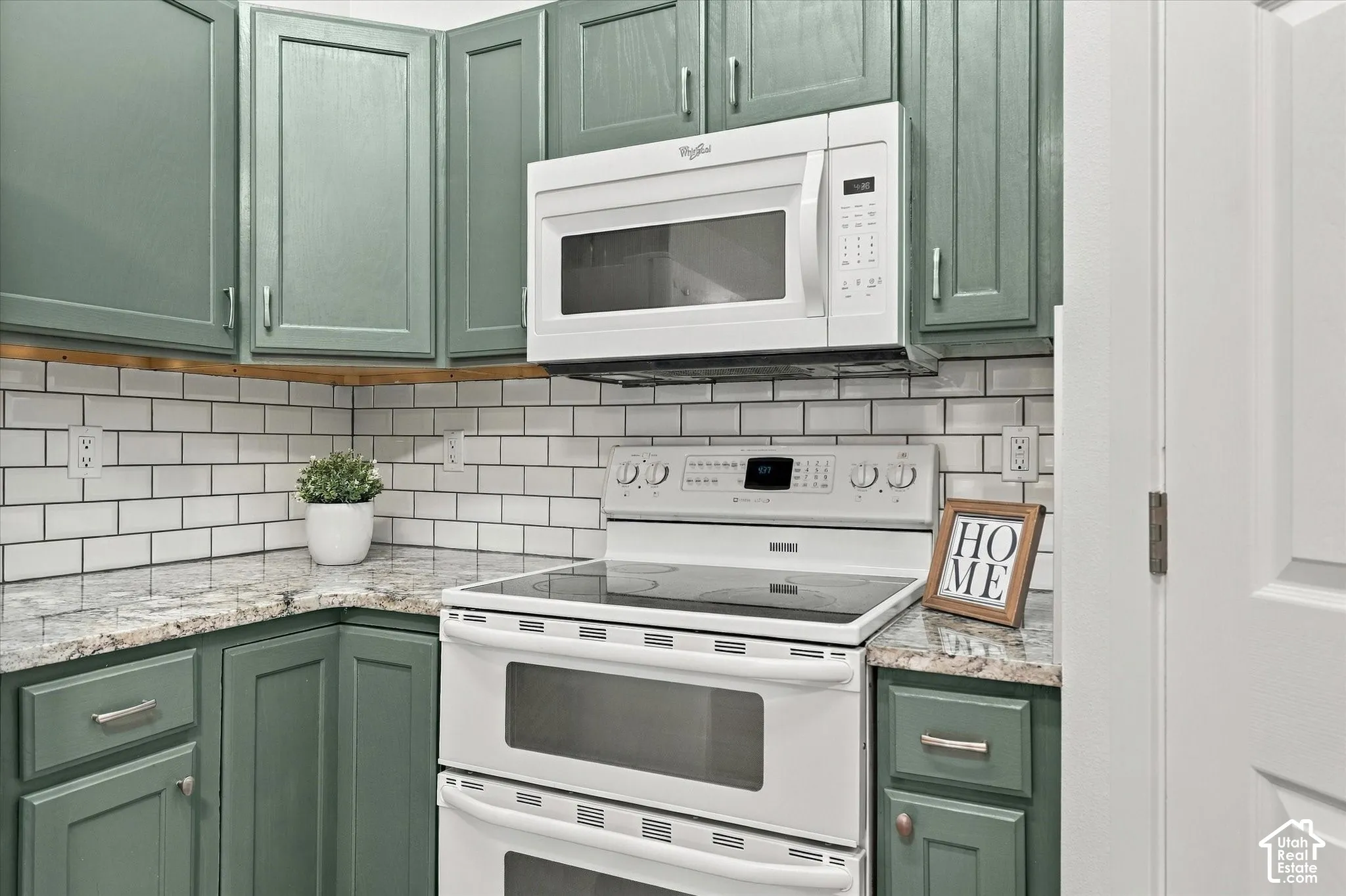 Kitchen featuring a double oven range, built-in microwave, subway tile backsplash, green cabinetry, and light-toned countertops