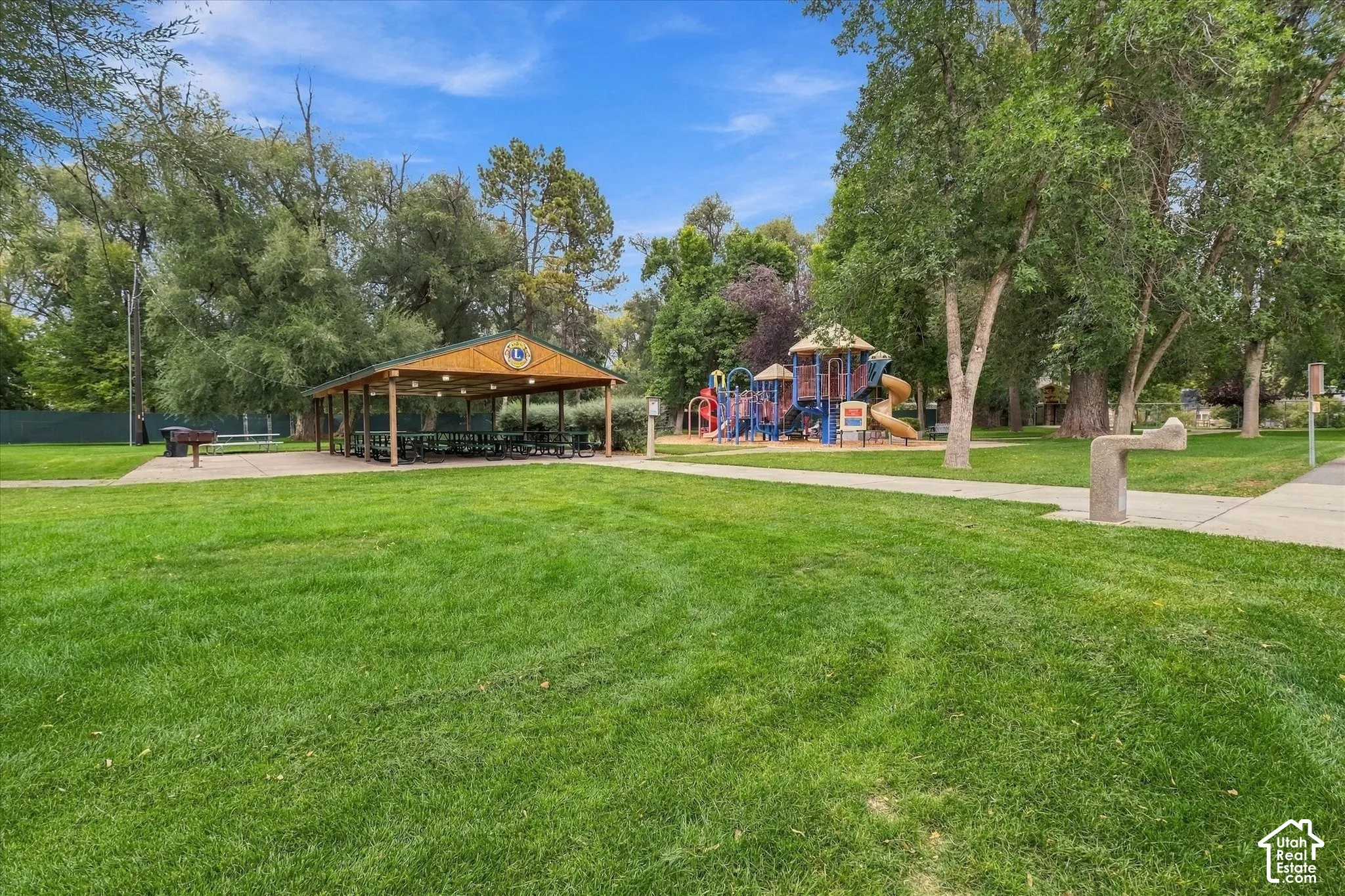 Expansive grassy area featuring a covered picnic pavilion, playground structure, and mature trees