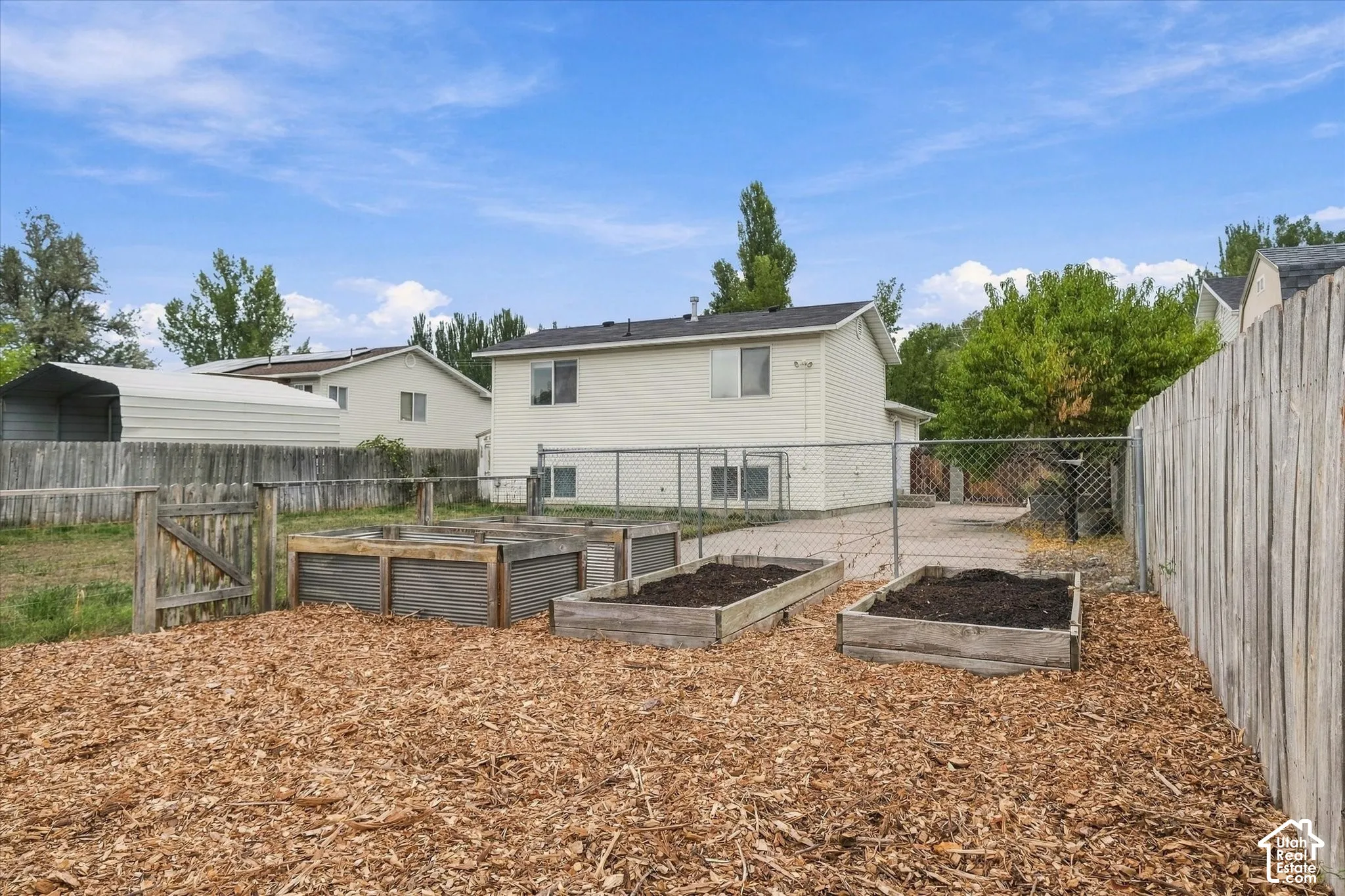 Fenced backyard featuring three raised garden beds, wood chip ground cover, and a wooden privacy fence
