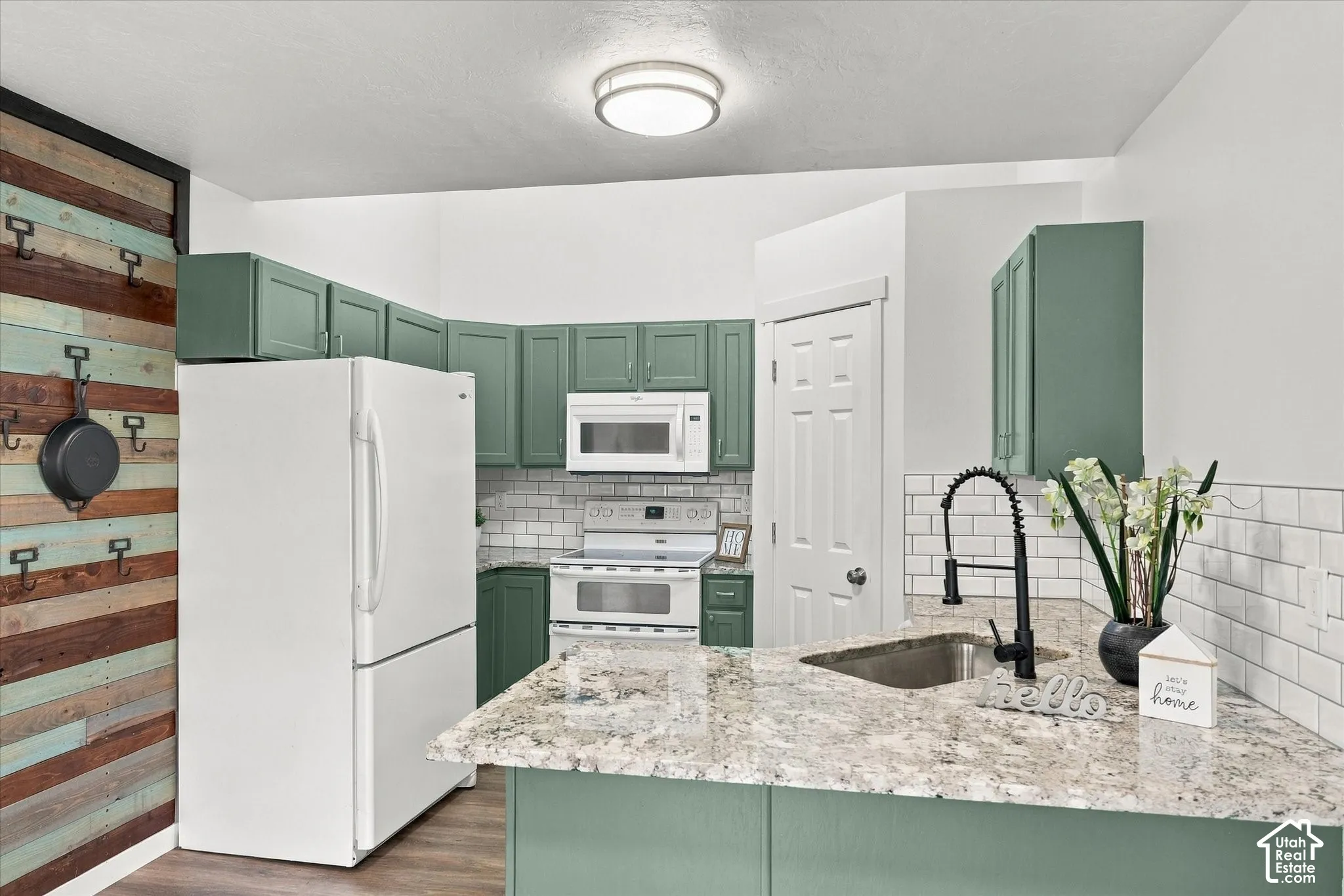 Kitchen featuring green cabinetry, white subway tile backsplash, a stainless steel sink, and light-toned countertops