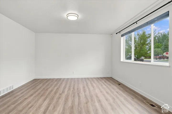 Spacious room with wood-finish flooring, white walls, and a contemporary flush-mount ceiling light