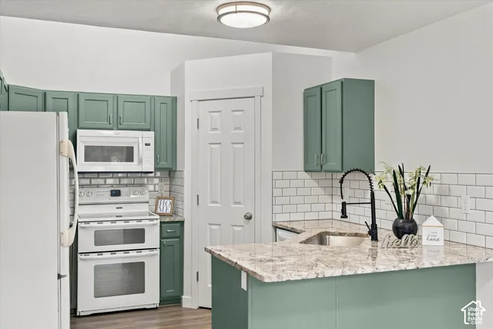 Kitchen featuring sage green cabinetry, white subway tile backsplash, light-colored stone-finish countertops, and a black gooseneck faucet