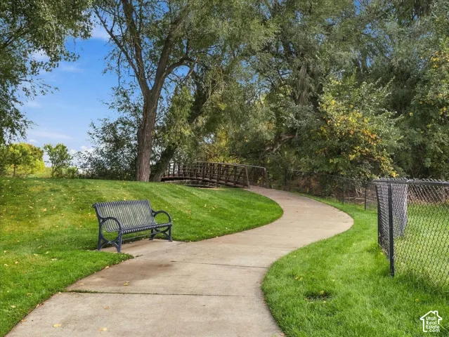 Manicured lawn with mature trees, a concrete pathway, and a decorative metal bench