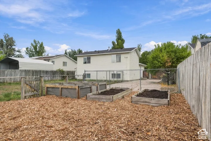 Fenced backyard featuring three raised garden beds, wood chip ground cover, and a wooden privacy fence