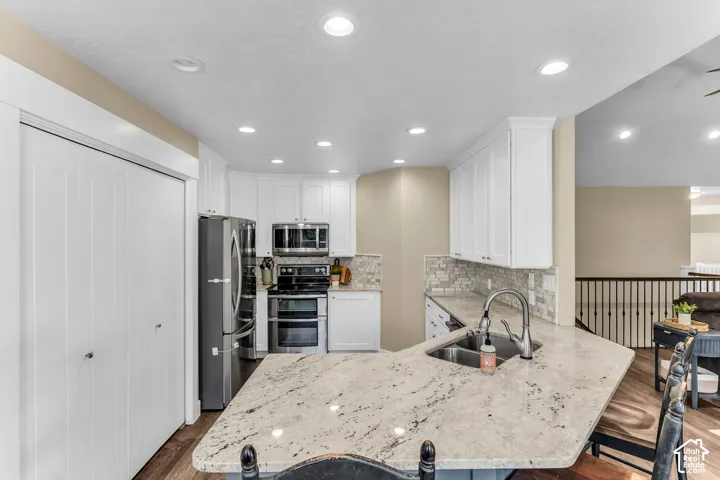 Kitchen featuring white cabinetry, stainless steel appliances, a tile backsplash, and a large island with a double basin sink and stone countertop