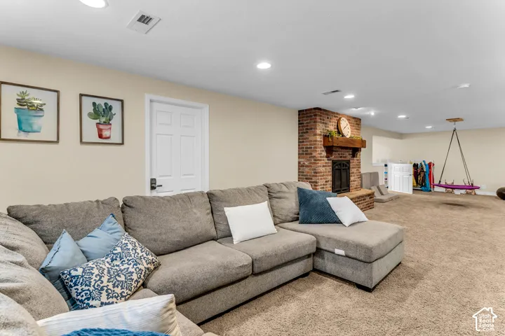 Expansive carpeted room featuring a brick fireplace with a wood mantle, recessed lighting, and a white panel door with black hardware