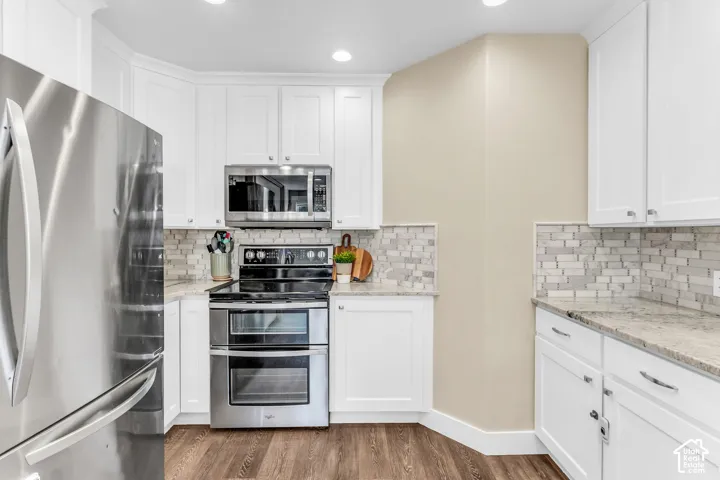 White shaker cabinetry with chrome hardware, stainless steel appliances, mosaic tile backsplash, light-toned countertops, and wood-finish flooring