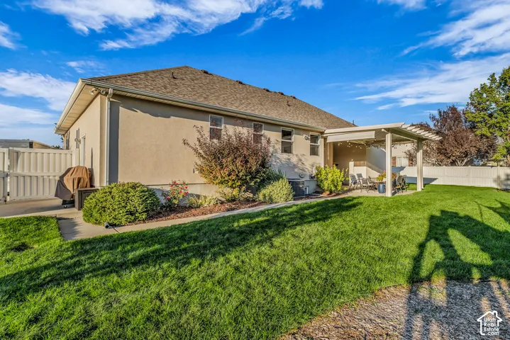 Expansive backyard featuring a manicured lawn, established landscaping, privacy fencing, and a covered patio with a pergola