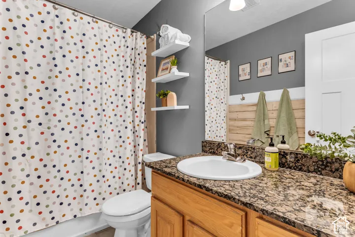 Bathroom featuring a vanity with a drop-in sink, dark speckled countertop, wood-finish cabinetry, and a large wall-mounted mirror
